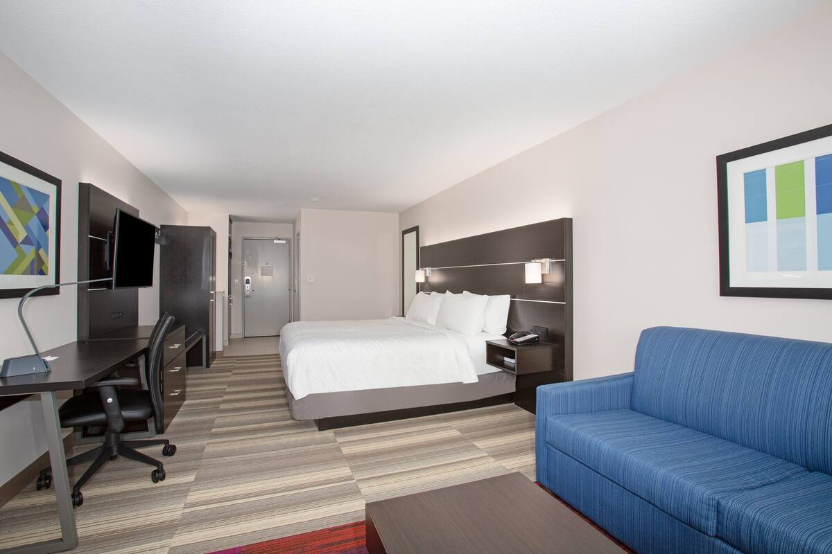 A hotel room with a bed, a desk with a chair, a blue sofa, and a TV on a stand.