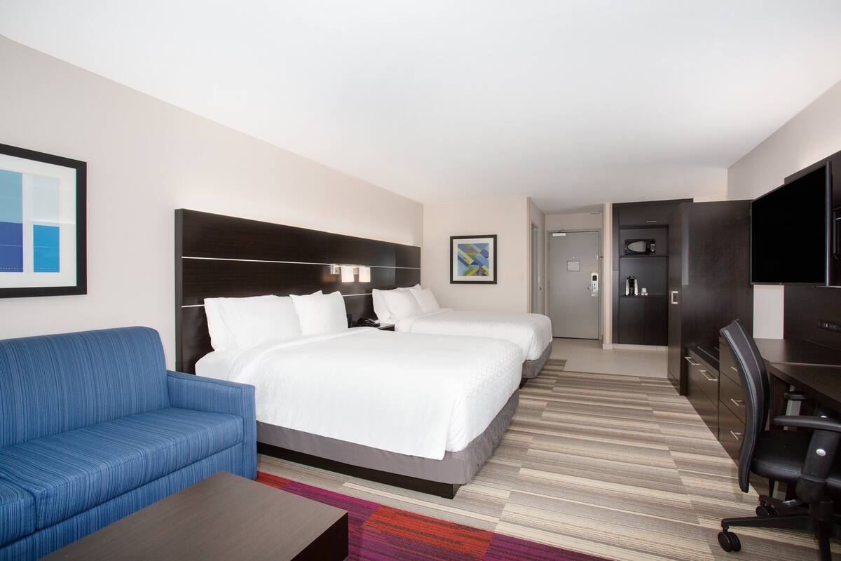 A hotel room with a large bed, a blue sofa, a desk, and a television.