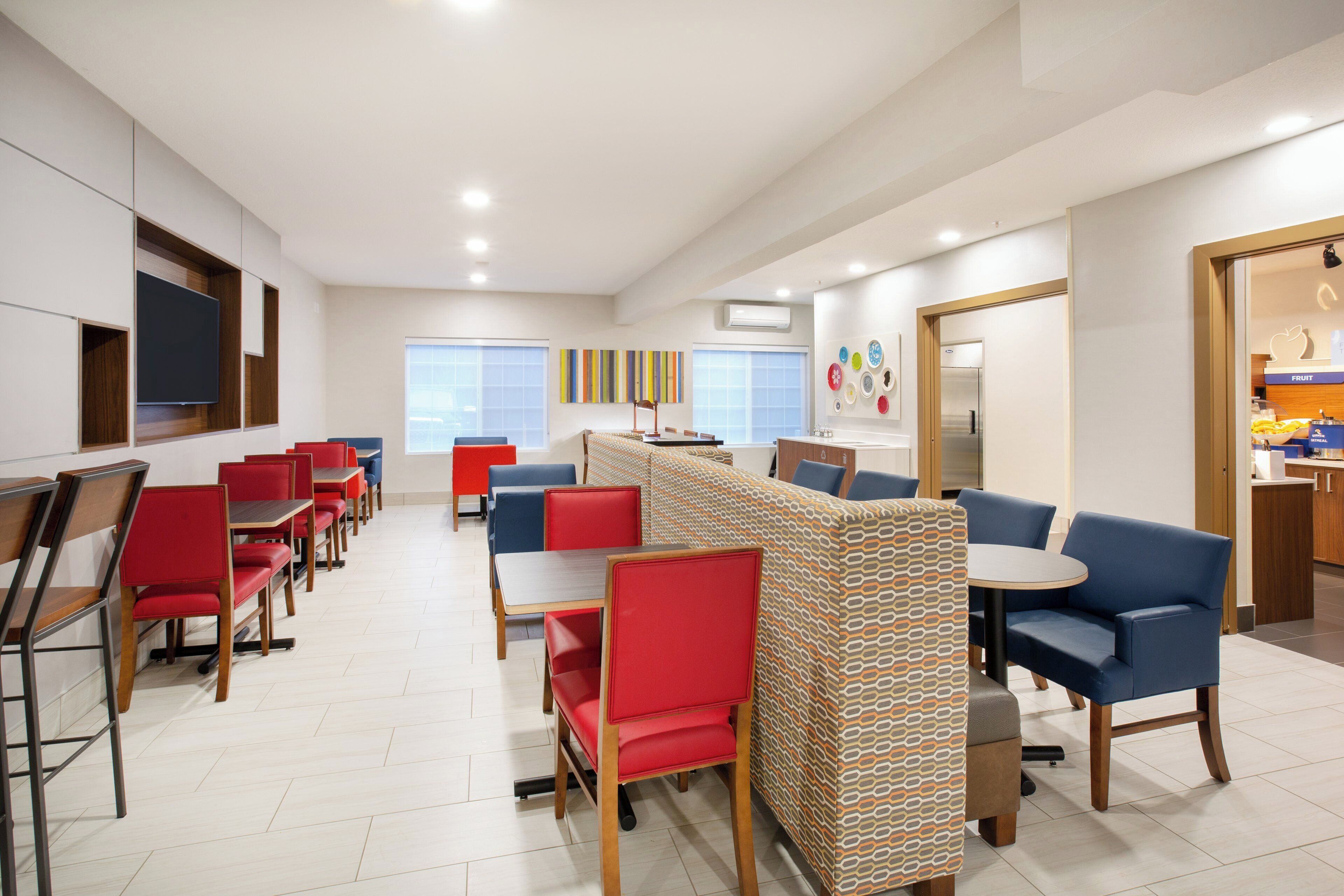 A modern dining area with red and blue seating, a patterned partition, and a kitchen area with a fruit display.