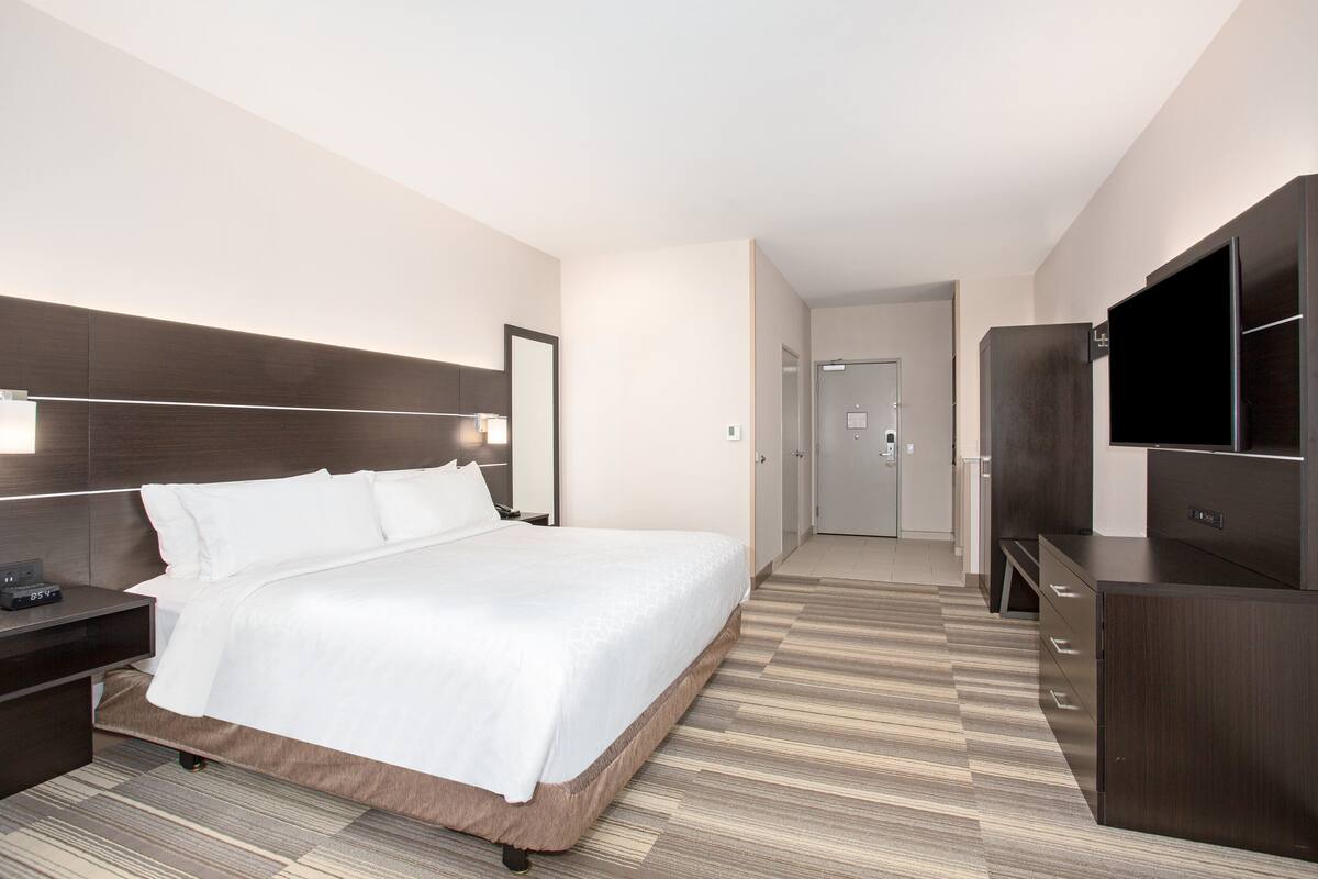 A modern hotel room with a large bed, a bedside table, a TV, and a wardrobe.