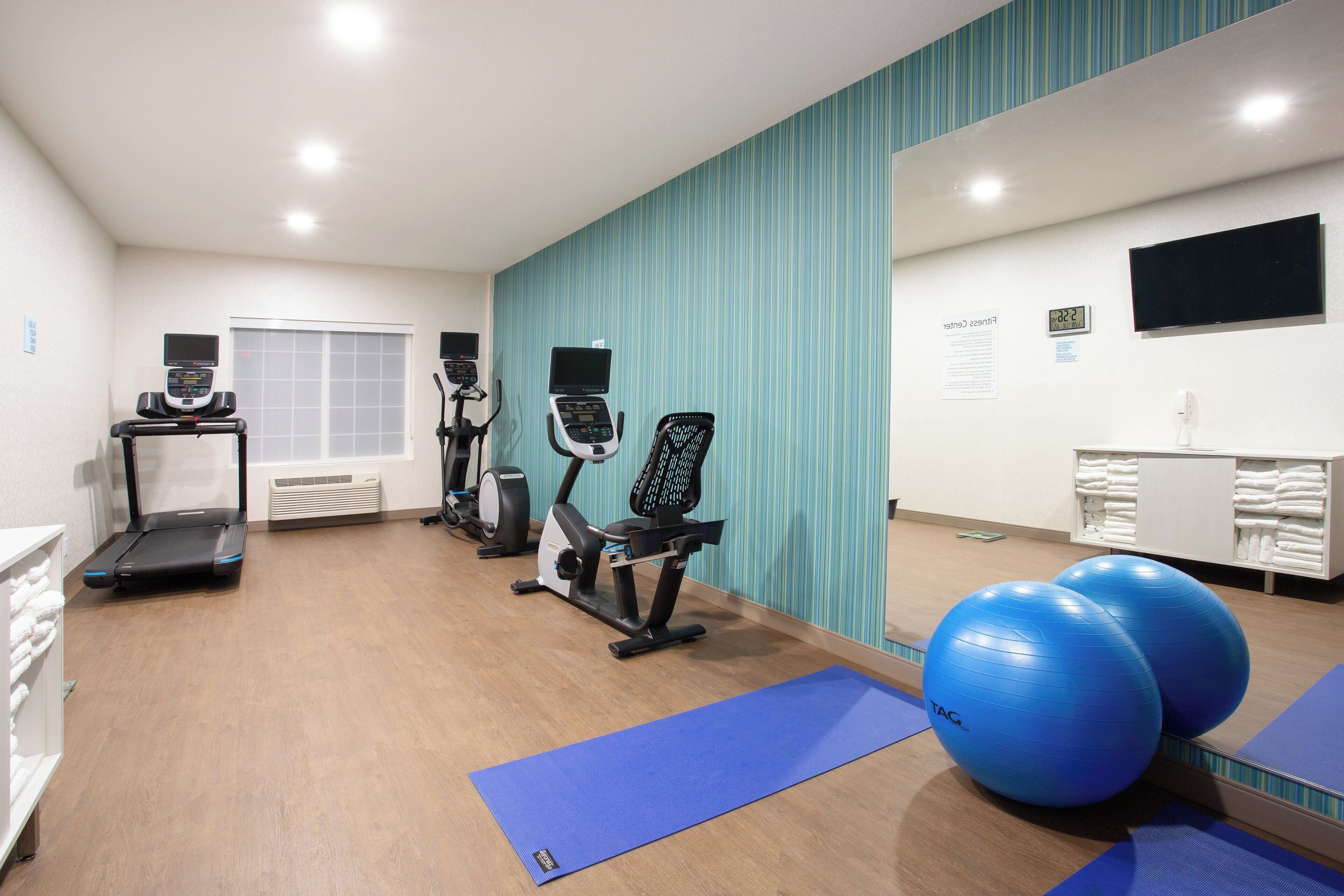 A gym with exercise equipment, a treadmill, stationary bikes, and exercise balls.
