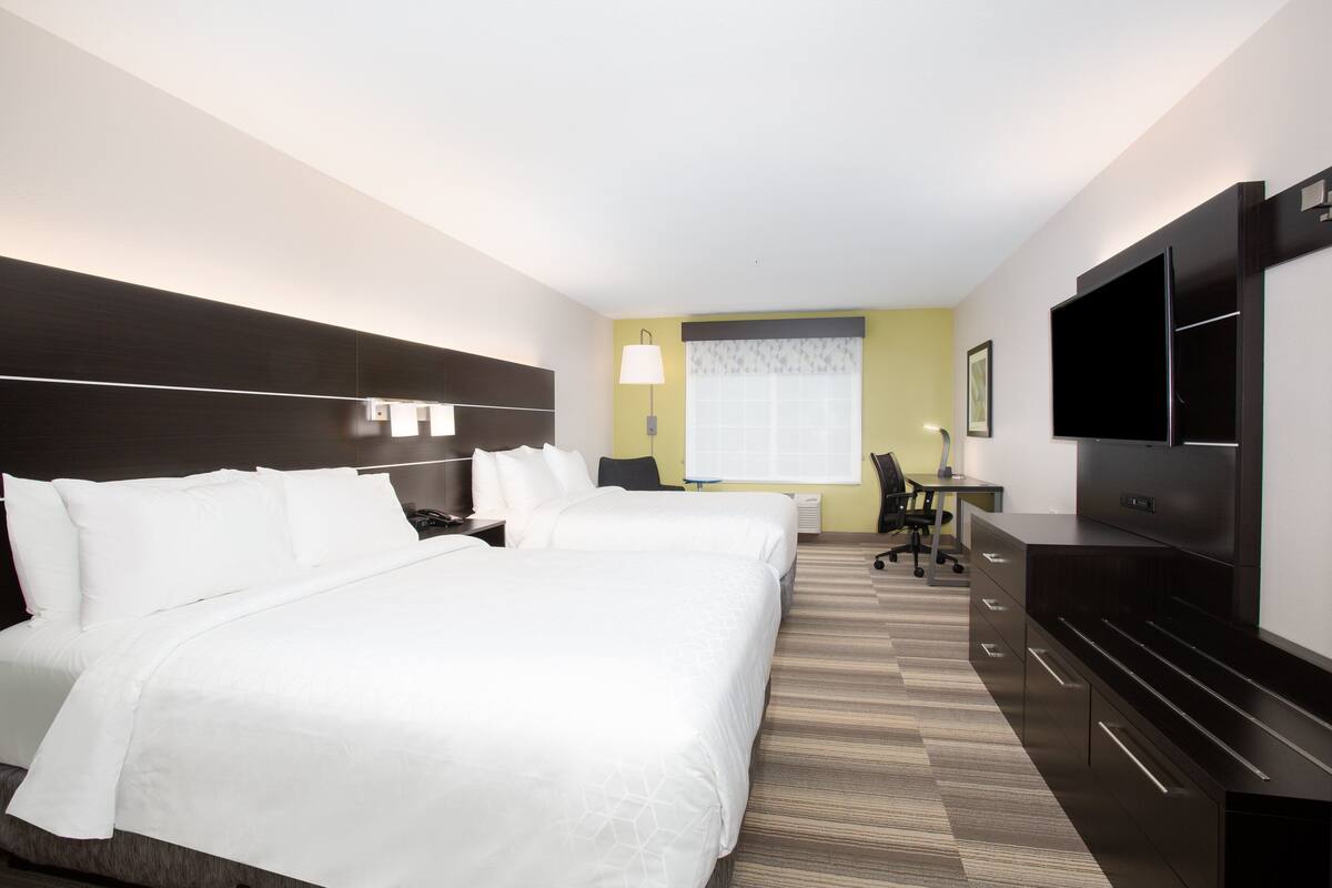 A hotel room with two beds, a desk, a chair, a flat-screen TV, and a lamp.