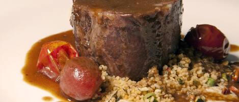 A plate with a piece of meat, a sausage, and a grain dish.