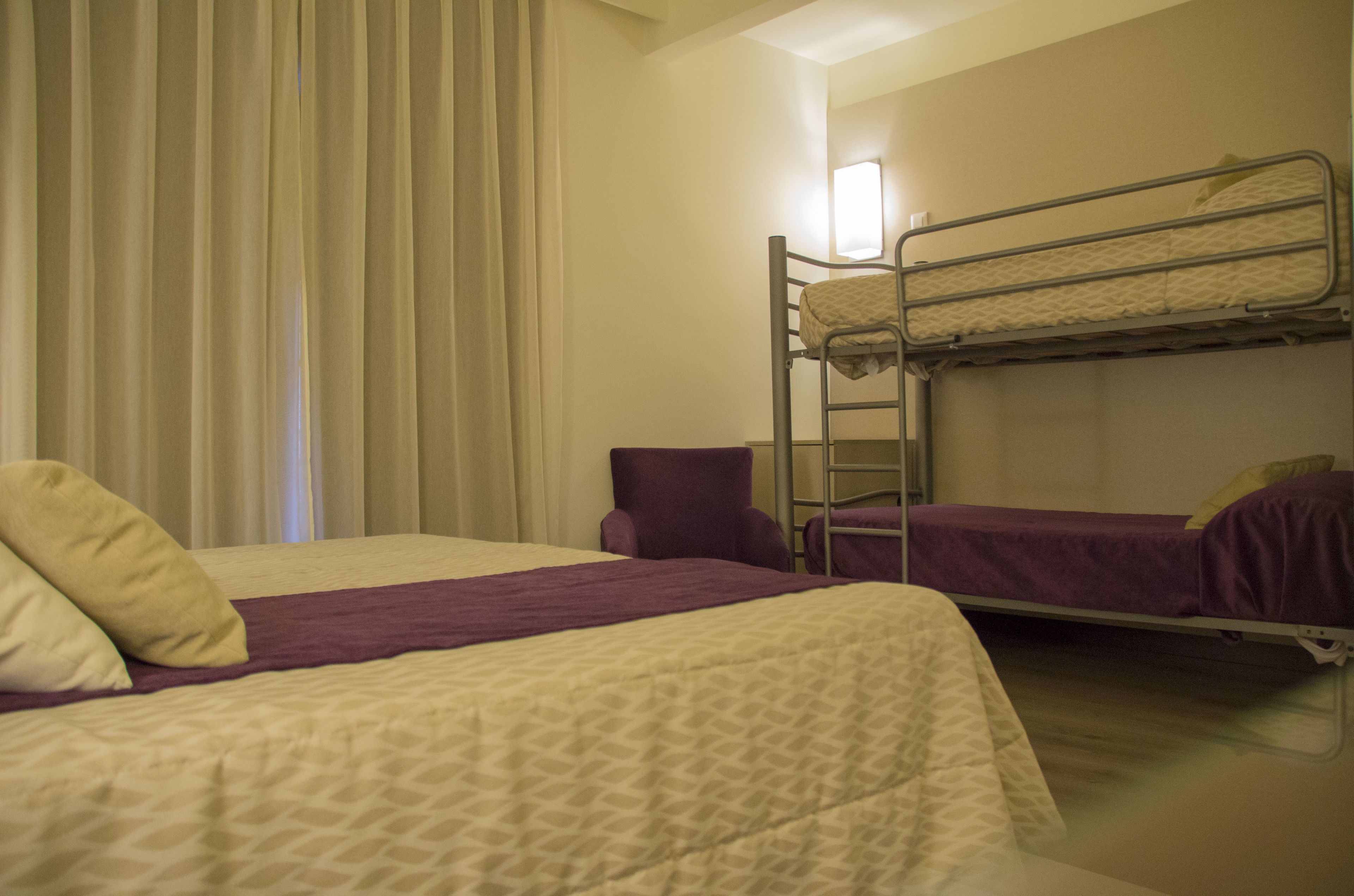 Una habitación con dos literas, un almohá de color púrpura y una ventana con cortinas.