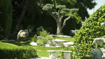 Un jardín bien cuidado con un árbol grande, bancos de piedra y diferentes arbustos.