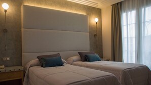 Une chambre d’hôtel avec deux lits, une grande tête de lit rembourrée, des lampes de chevet et une fenêtre avec des rideaux.