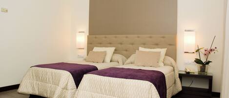 A double bed with a tufted headboard, two bedside tables with lamps, and a nightstand with a vase of flowers.