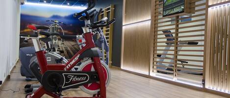 A gym with stationary bikes, a treadmill, and a wall-mounted TV.