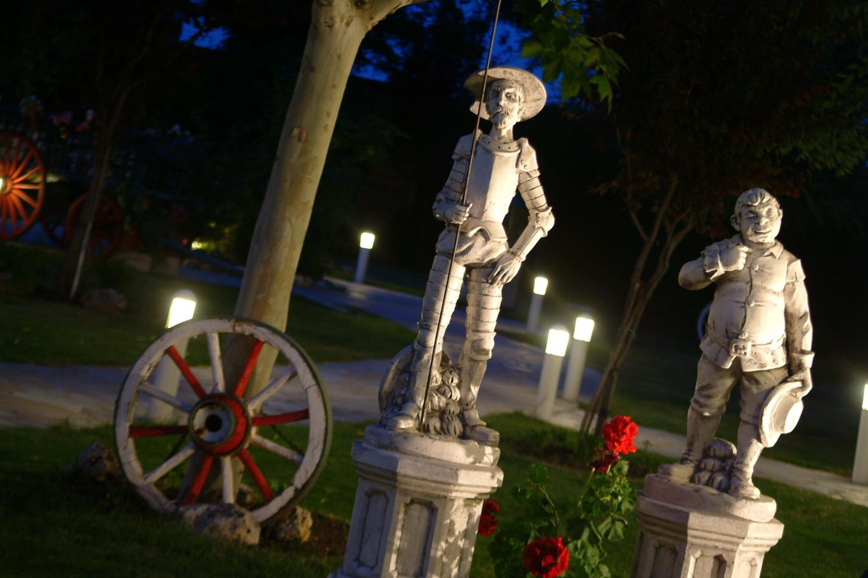 Una estatua de un hombre con armadura y espada, sobre un pedestal en un parque de noche.