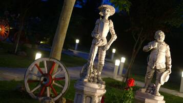 Una estatua de un hombre con armadura y espada, sobre un pedestal en un parque de noche.
