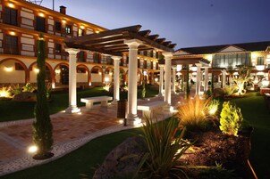 Un patio con una pérgola, bancos y jardines bien cuidados.