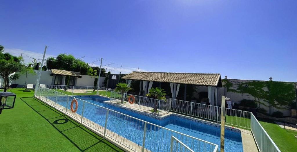 Una piscina con zona vallada, un flotador salvavidas y una zona de estar techada.