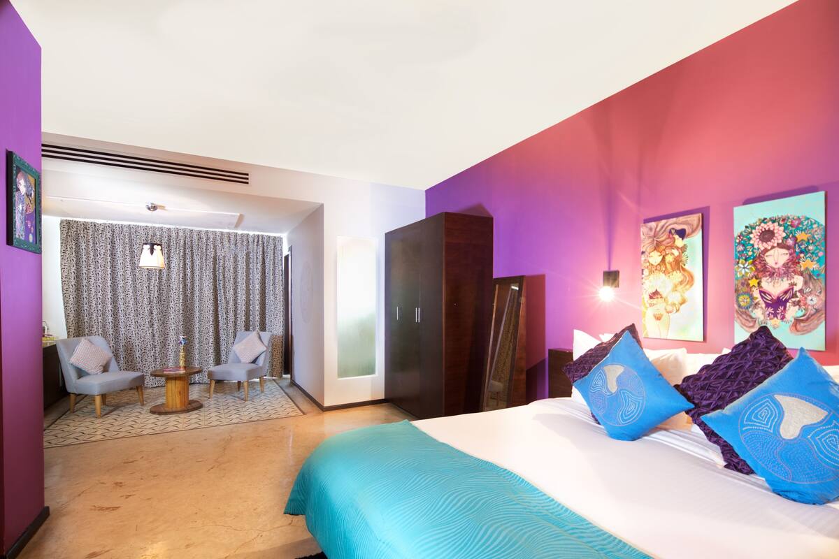 Une chambre d’hôtel moderne comprenant un lit, deux fauteuils, une petite table et une armoire.