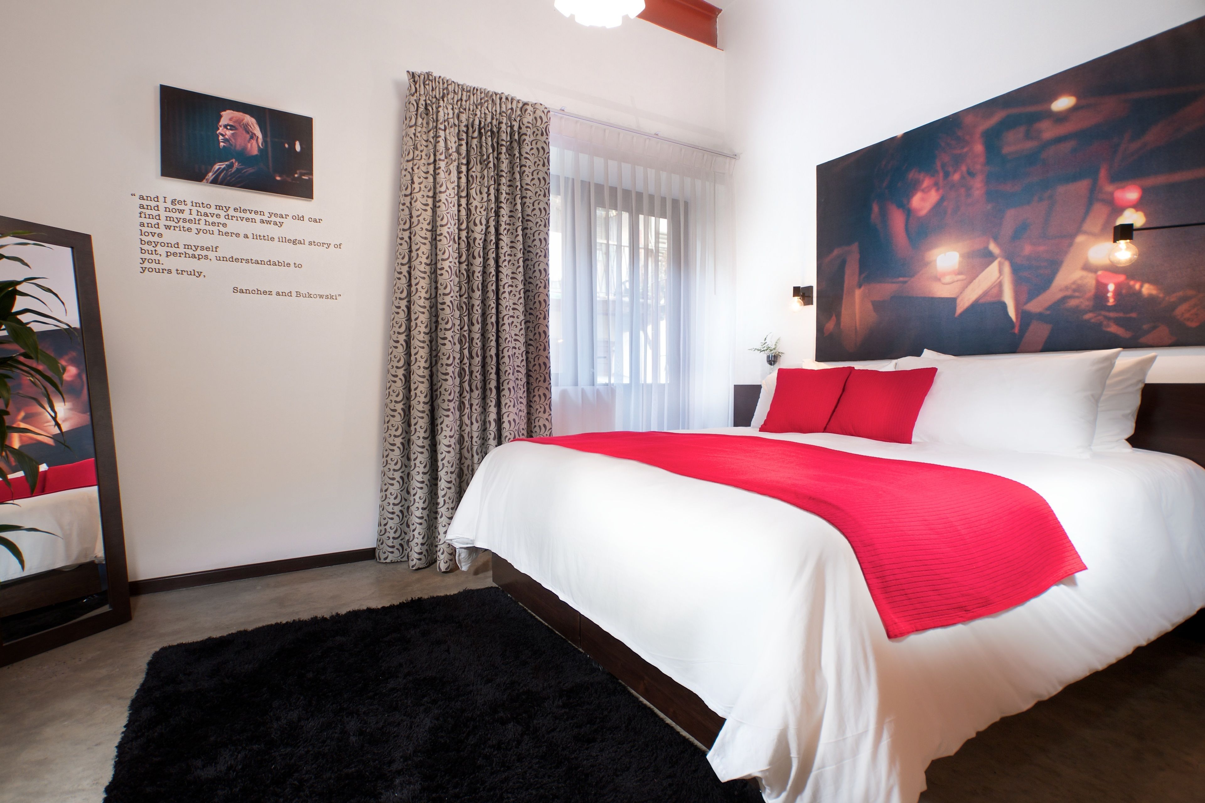 A modern hotel room with a large bed, a black rug, a red throw, and a painting on the wall.