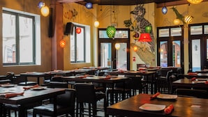 L’intérieur d’un restaurant, avec ses tables et ses chaises, ses luminaires décoratifs suspendus et une fresque murale.