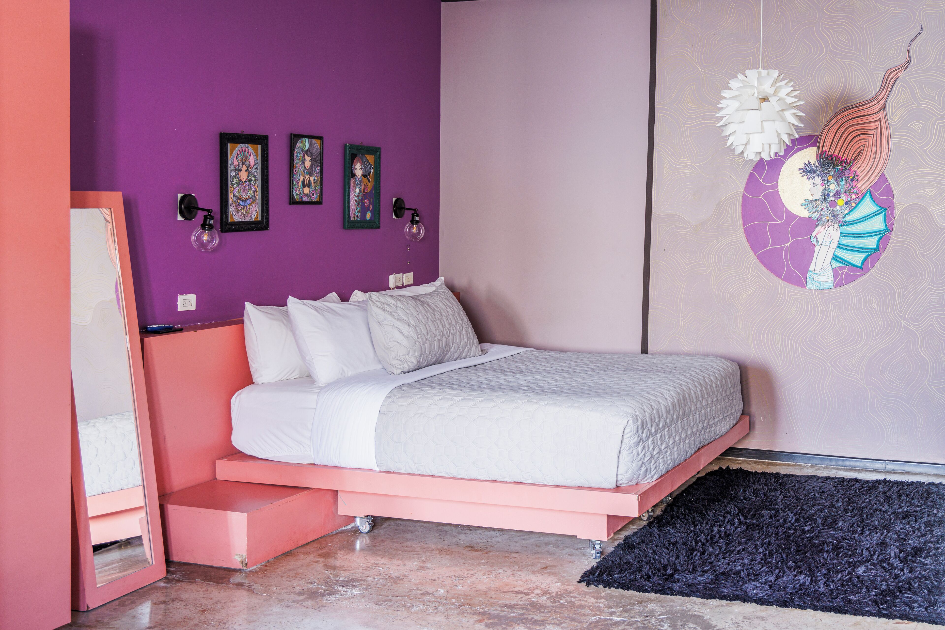 A bedroom with a pink bed frame, white bedding, and a purple wall with artwork.