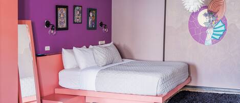 A bedroom with a pink bed frame, white bedding, and a purple wall with artwork.