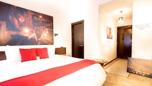 Une chambre d’hôtel avec un grand lit, un tableau au mur, une porte et une petite table avec une lampe.