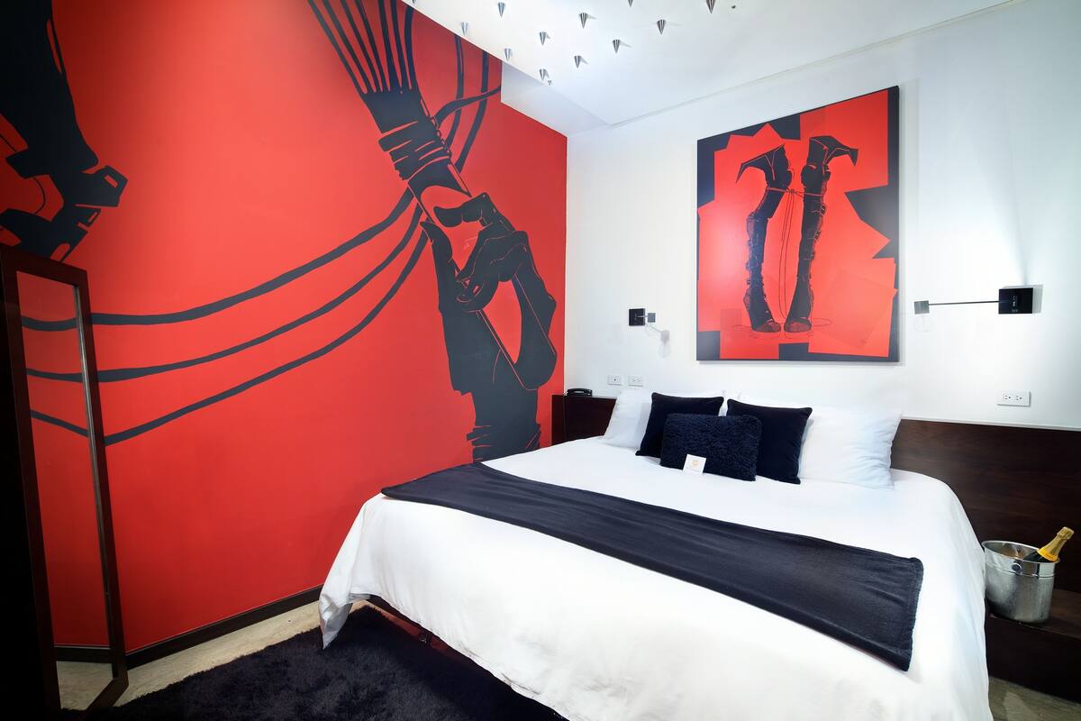 Une chambre d’hôtel moderne avec un grand lit, un mur d’accent rouge et des œuvres d’art abstraites.