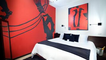 A modern hotel room with a large bed, a red accent wall, and abstract artwork.