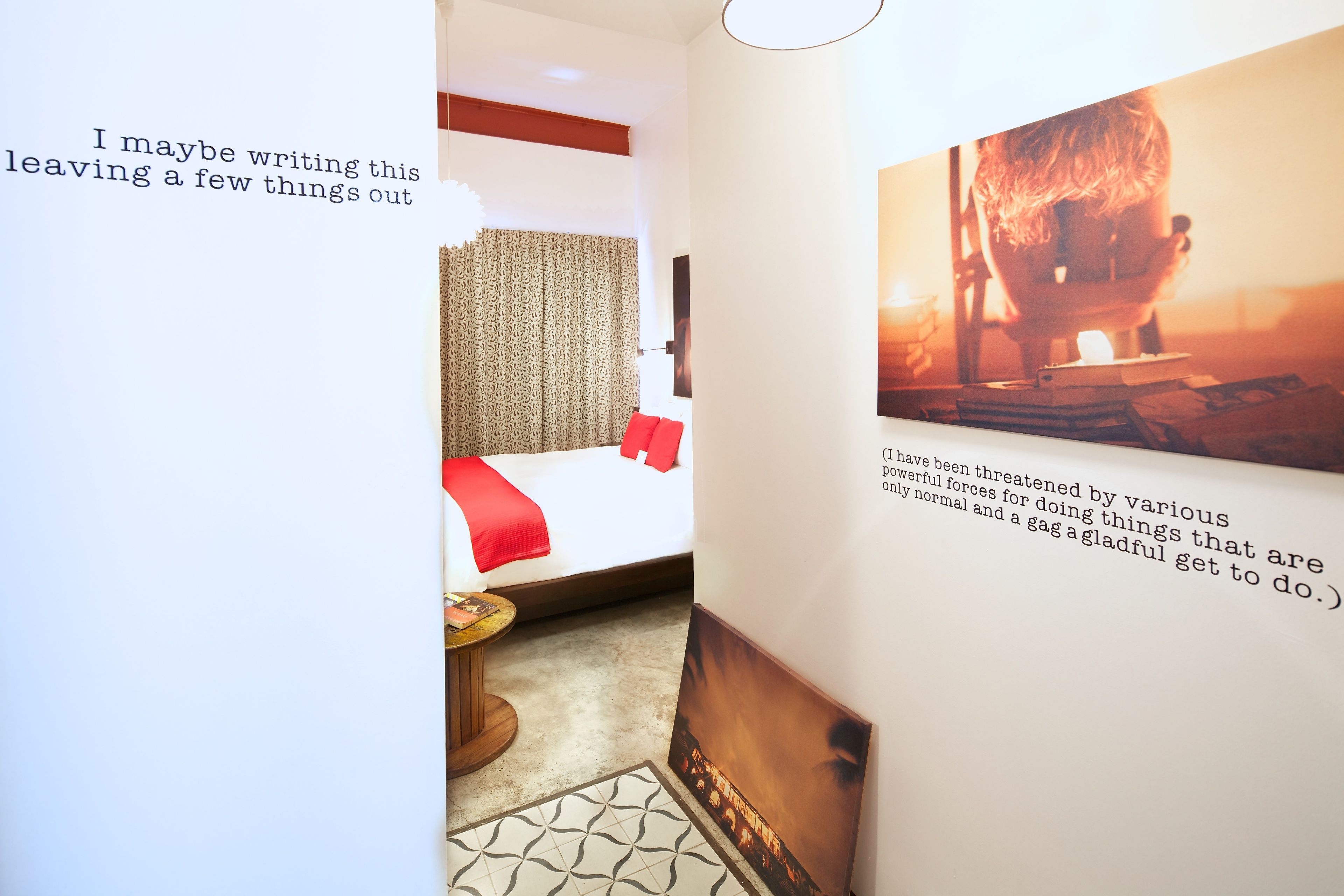 A hotel room with a bed, a small table, and a wall with a framed picture and text.