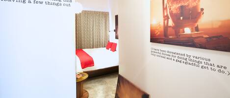 A hotel room with a bed, a small table, and a wall with a framed picture and text.
