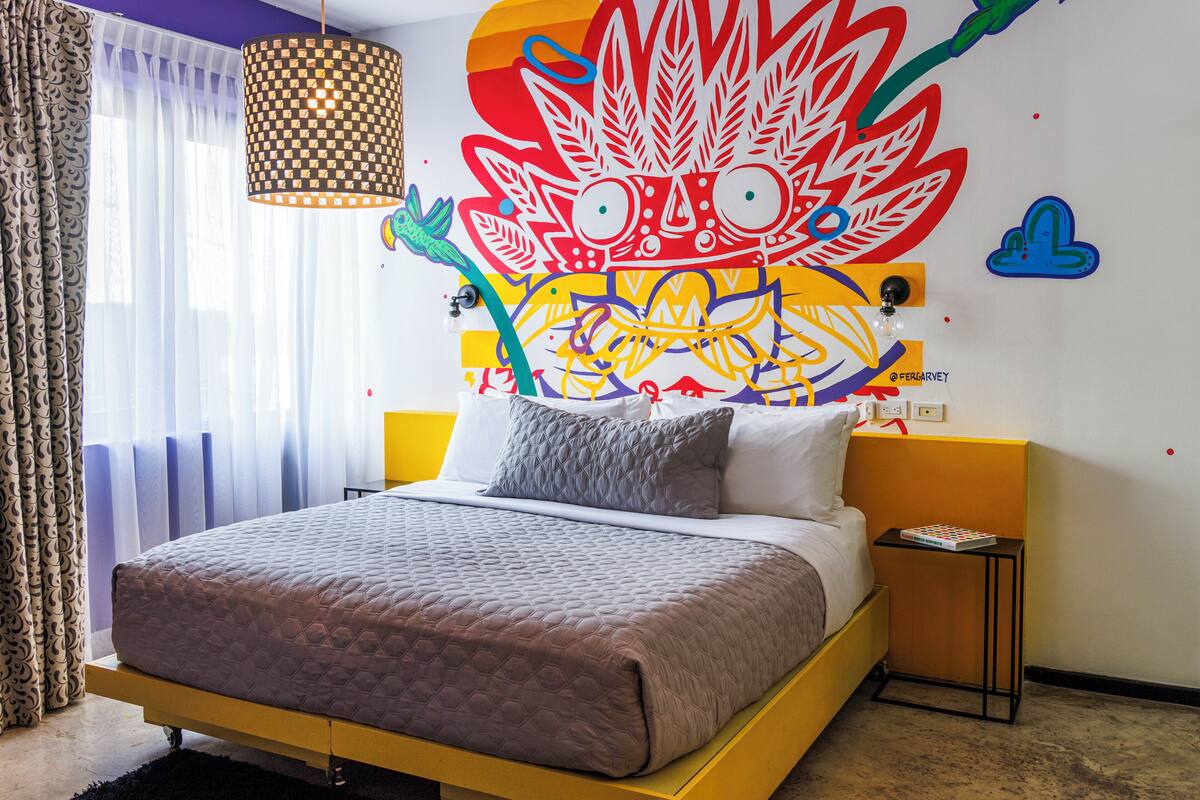 Une chambre à coucher moderne avec un lit, une fresque murale, une lampe et une petite table de chevet.