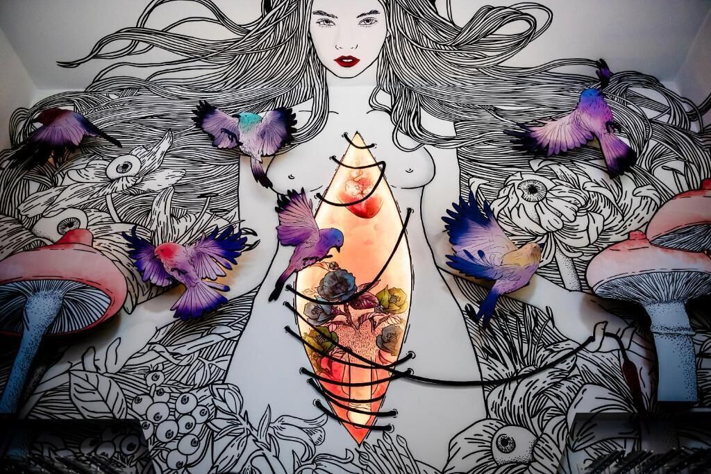 Un mural detallado con una figura central rodeada de diversos elementos como pájaros, flores y hongos.