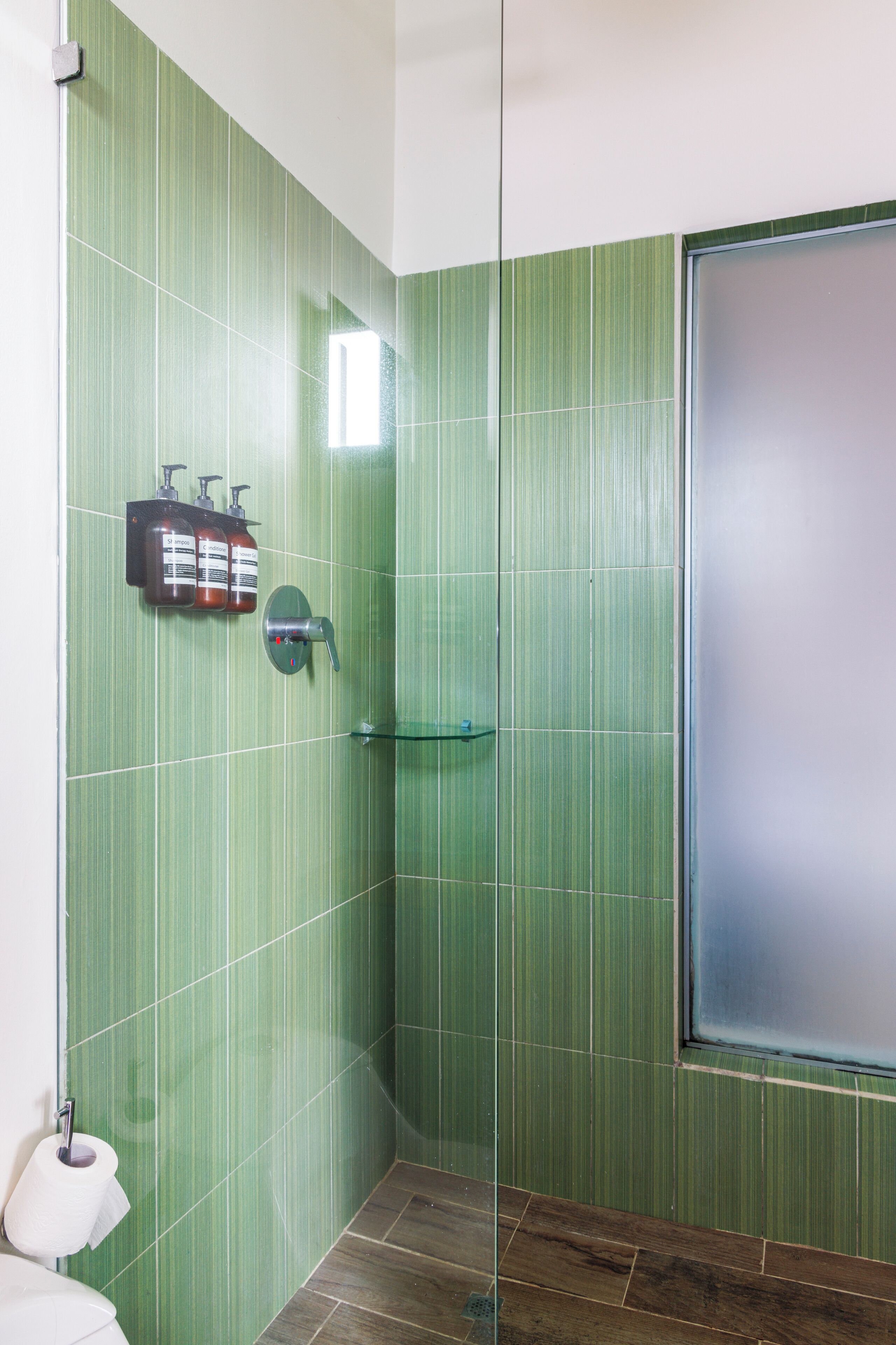 A bathroom with green tiled walls, a glass shower enclosure, a toilet, and a hand dryer.