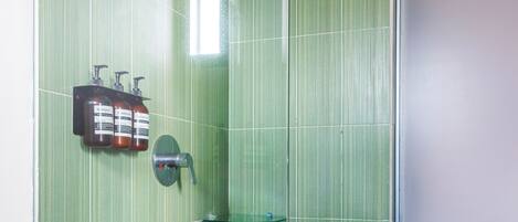 A bathroom with green tiled walls, a glass shower enclosure, a toilet, and a hand dryer.