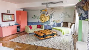 Une pièce comprenant un coin cuisine, un canapé, un lit et une fresque murale sur laquelle est inscrite la phrase « Respirez simplement ».