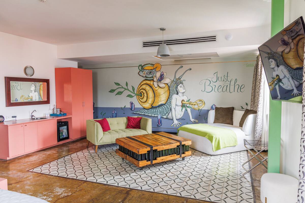 Une pièce comprenant un coin cuisine, un canapé, un lit et une fresque murale sur laquelle est inscrite la phrase « Respirez simplement ».