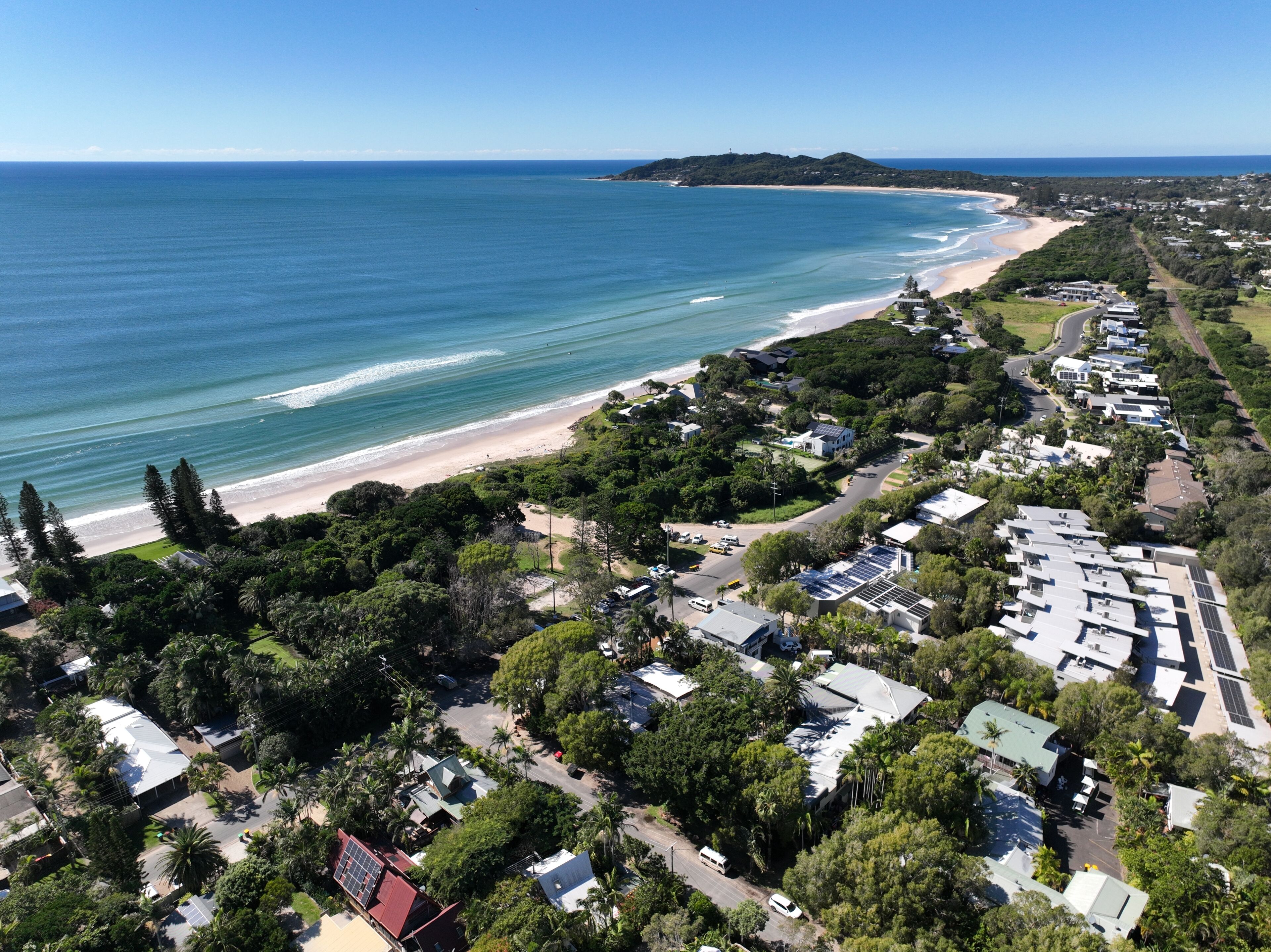 An aerial view of a coastal area with a beach, residential buildings, and greenery.