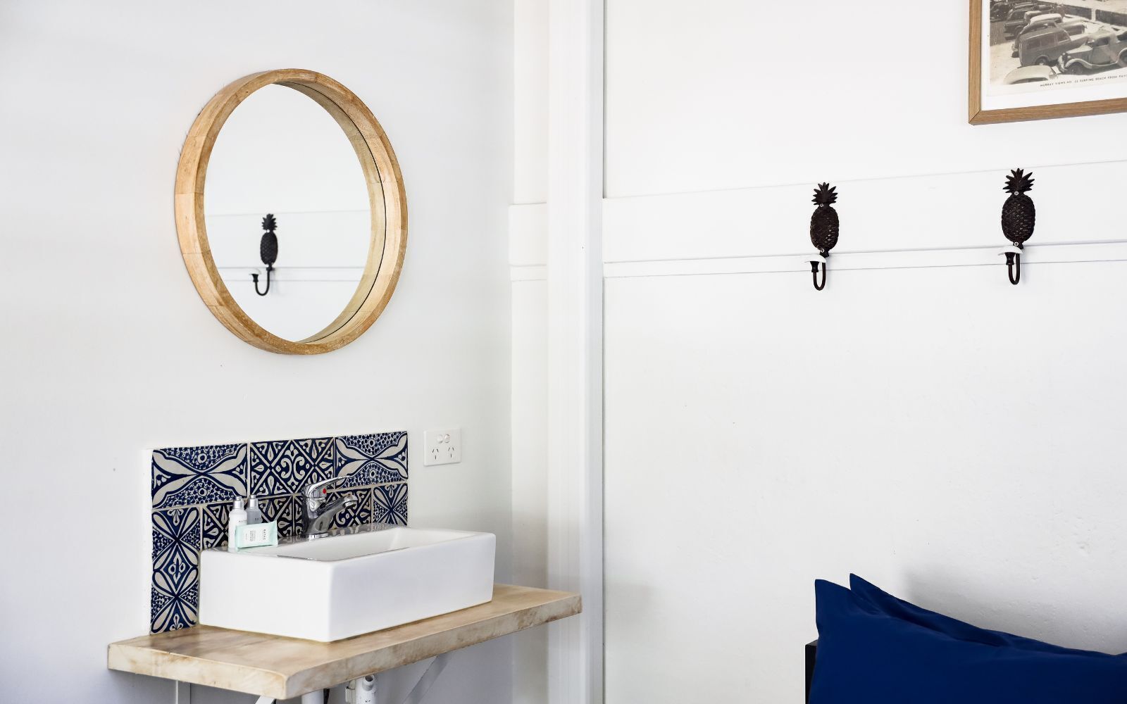 Un baño con espejo de marco de madera, lavabo blanco y un salpicadero con diseño, además de un perchero con ganchos decorativos.