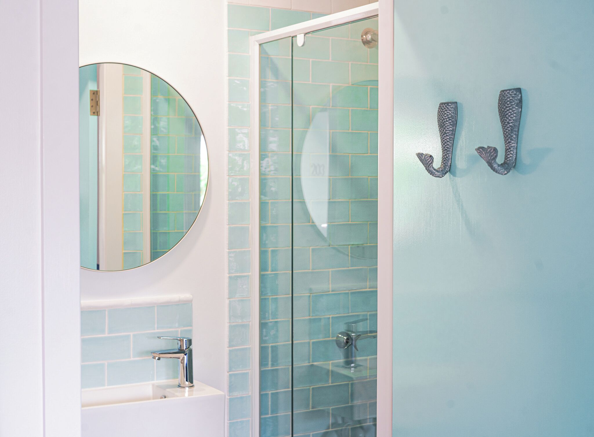 A bathroom with a round mirror, a sink, and a glass shower enclosure.