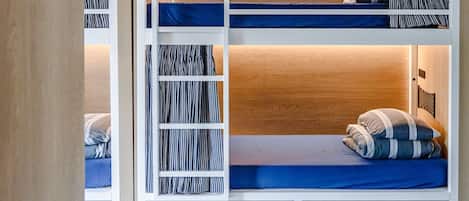 A bunk bed with a lower bunk, a shelf with striped bedding, and a drawer unit.