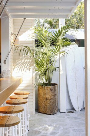 A bar area with stools, a potted plant, and a surfboard. - Wake Up! Byron Bay - Hostel (Byron Bay)