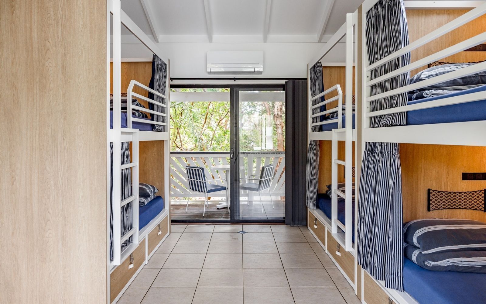 A room with bunk beds, a sliding glass door leading to an outdoor area with chairs, and a visible air conditioning unit.