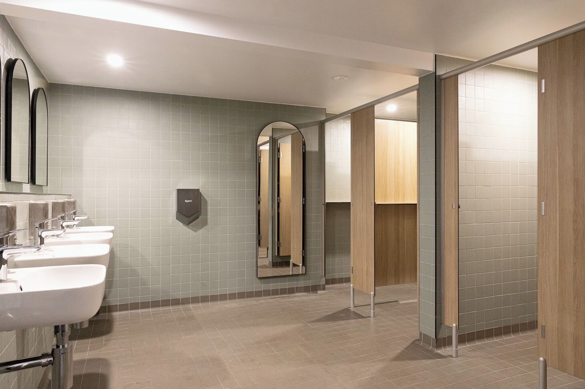 A modern restroom with three sinks, a hand dryer, and a mirror.