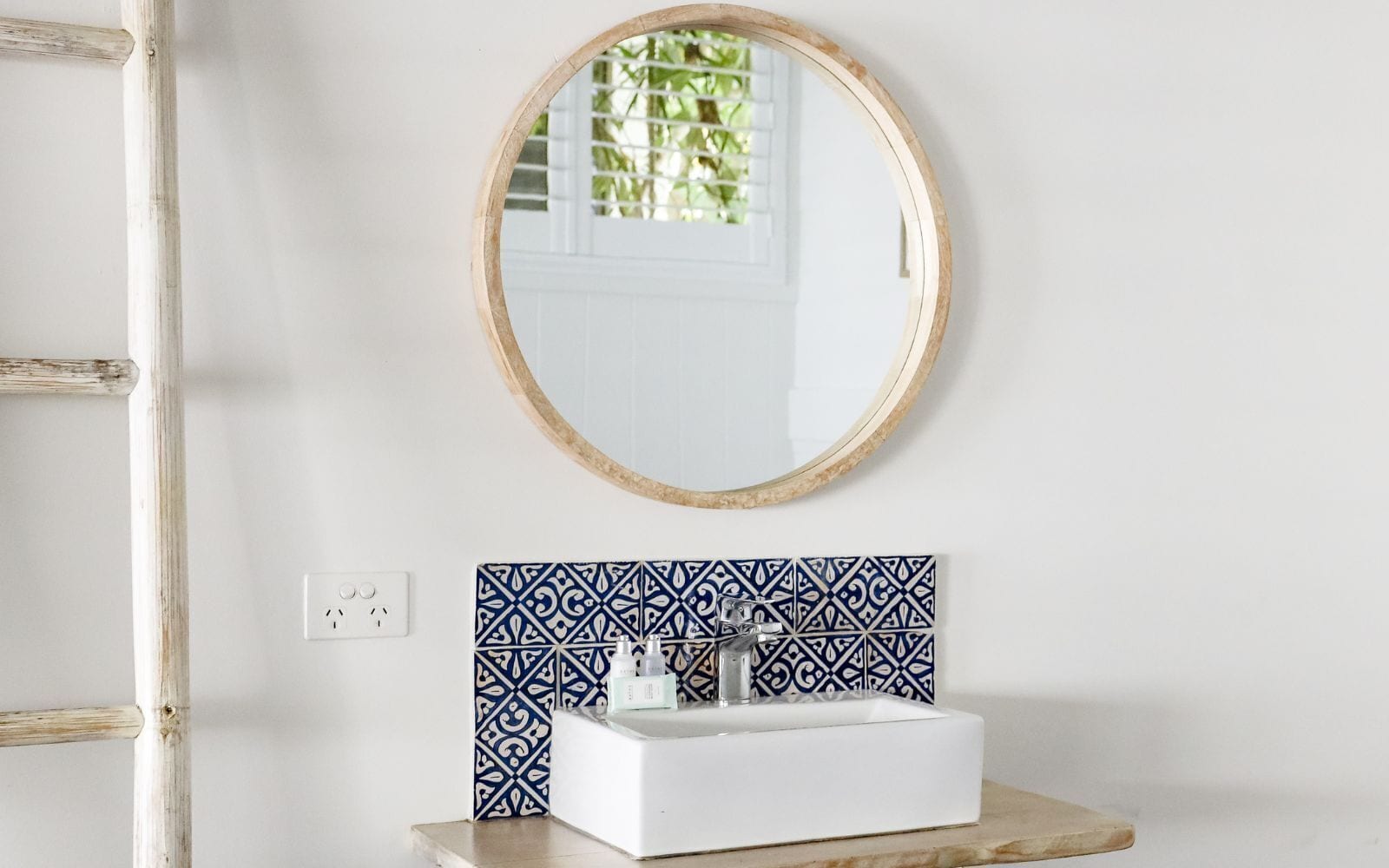 A bathroom with a white sink, a mirror with a wooden frame, and patterned tiles.