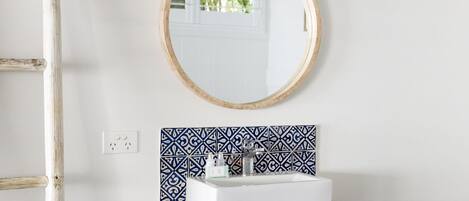 A bathroom with a white sink, a mirror with a wooden frame, and patterned tiles.