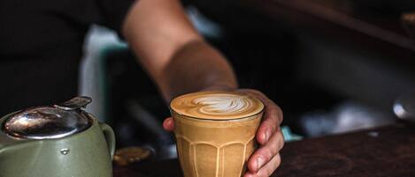 A person holding a cup with a latte art design, a green teapot, and a bar counter.