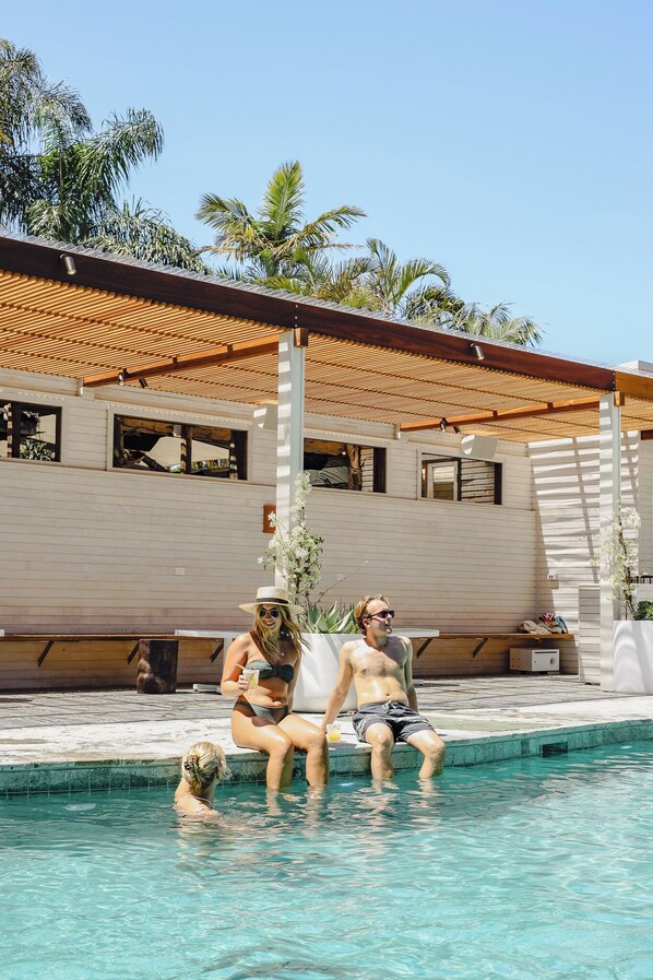 A swimming pool with a wooden deck and a building with large windows in the background. - Wake Up! Byron Bay - Hostel (Byron Bay)