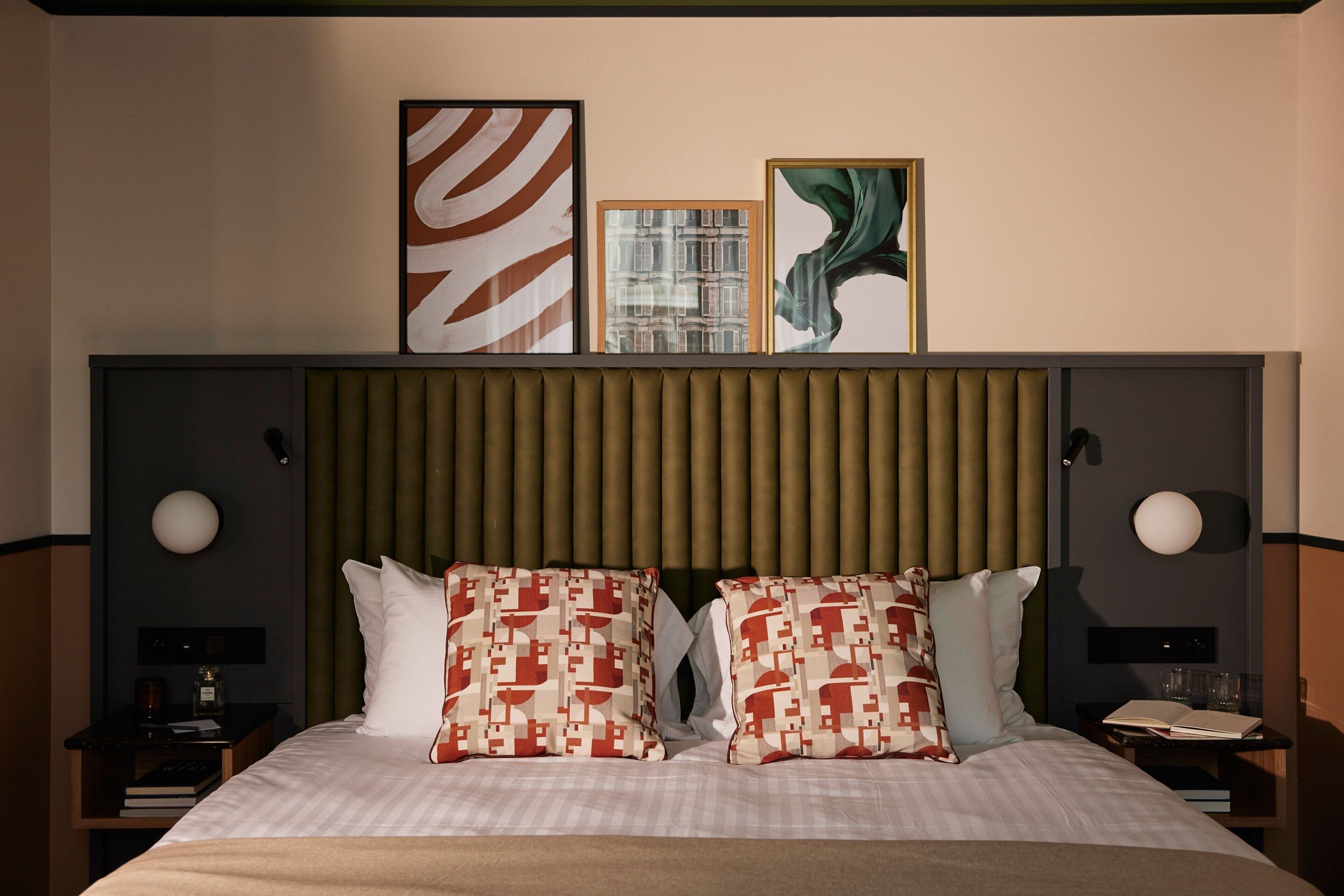 A hotel room with a large bed, two nightstands, a headboard with vertical slats, and three framed artworks on the wall.