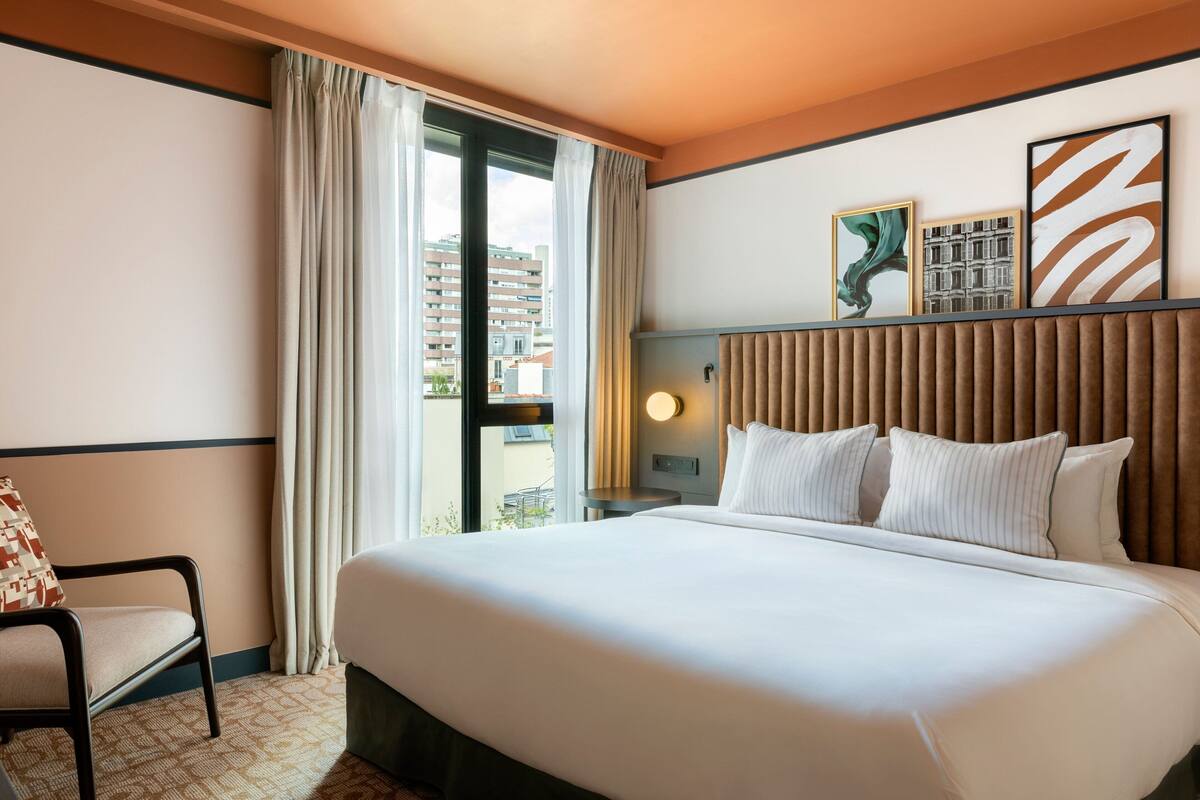 Une chambre d’hôtel avec un grand lit, une chaise, une table de chevet et une fenêtre avec des rideaux.