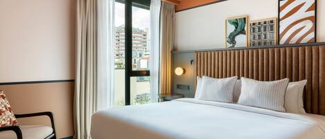 A hotel room with a large bed, a chair, a nightstand, and a window with curtains.