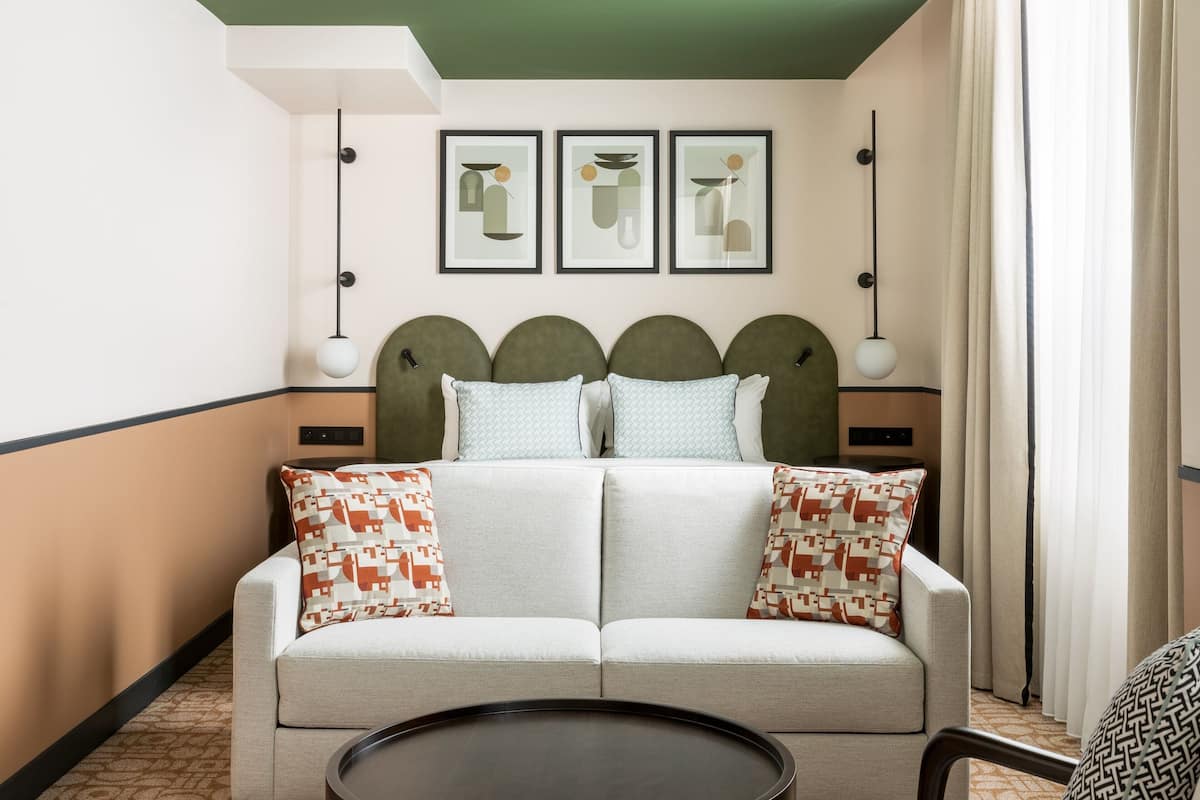 Une chambre d’hôtel avec un canapé, des coussins, une table ronde et des œuvres d’art encadrées accrochées au mur.