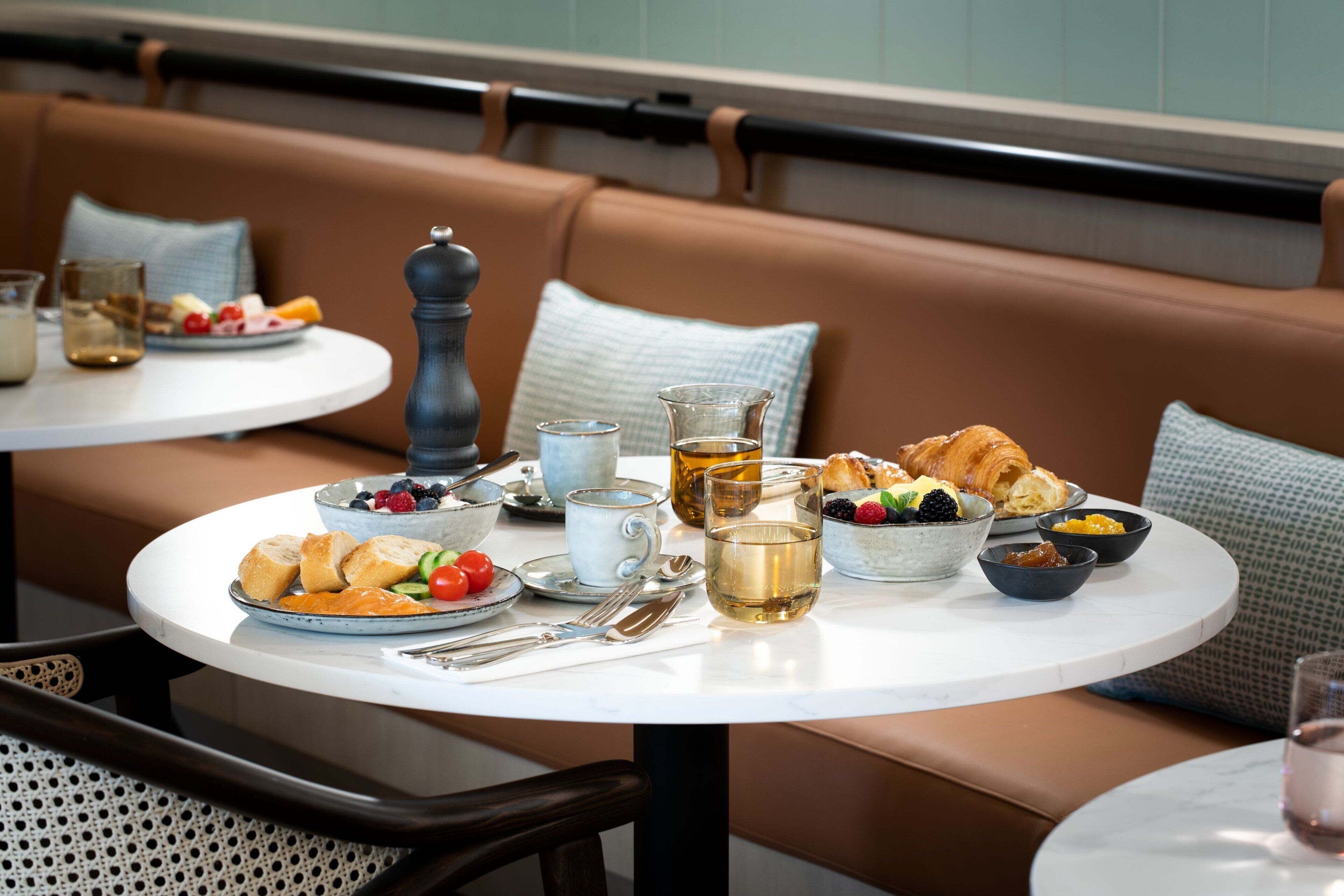 Une table à manger, dressée avec une variété de plats et de boissons, est placée sur une table ronde dans un coin salon agrémenté d’un banc marron rembourré.