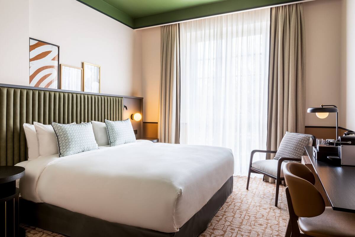 Une chambre d’hôtel avec un grand lit, un bureau, une chaise et une lampe.