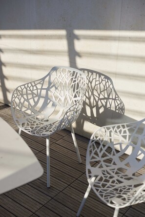 Dos sillas de metal blanco con diseño geométrico, ubicadas sobre una cubierta de madera.